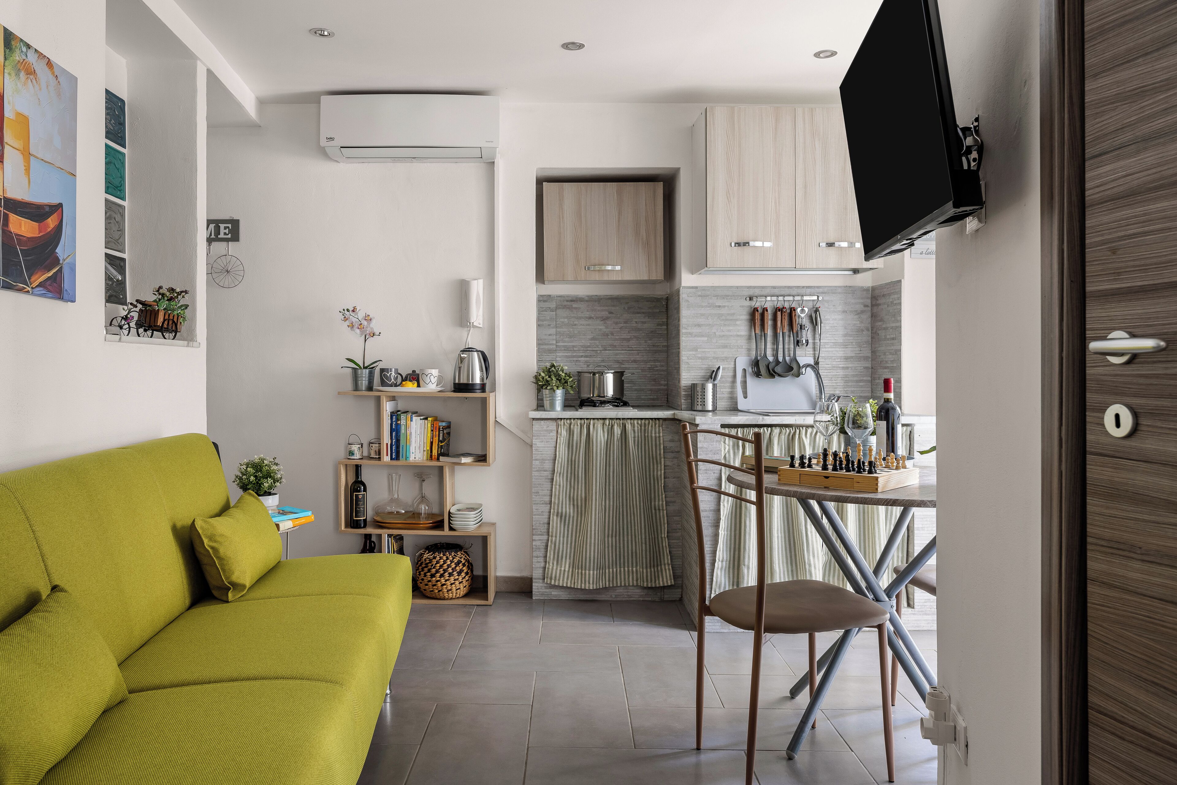 Un espace de vie compact comprenant un canapé, un coin repas avec une table et des chaises, une cuisine équipée de placards et un téléviseur fixé au mur.