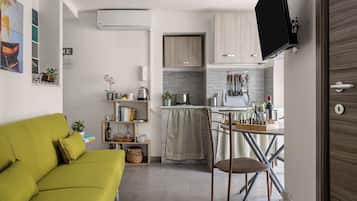 Un espace de vie compact comprenant un canapé, un coin repas avec une table et des chaises, une cuisine équipée de placards et un téléviseur fixé au mur.