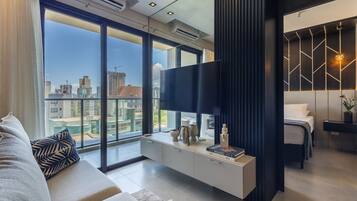 A modern bedroom with a large bed, a TV, and a city view.