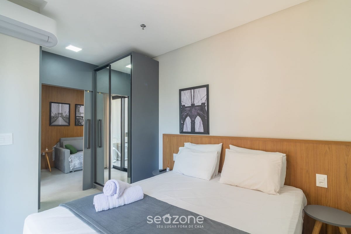 Een moderne hotelkamer met een groot bed, een klein nachtkastje, een kunstwerk aan de muur en uitzicht door een glazen deur naar een andere kamer.