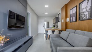 Una sala de estar moderna con un sofá gris, un televisor de pantalla plana y un comedor con una pared de madera y cuadros enmarcados.