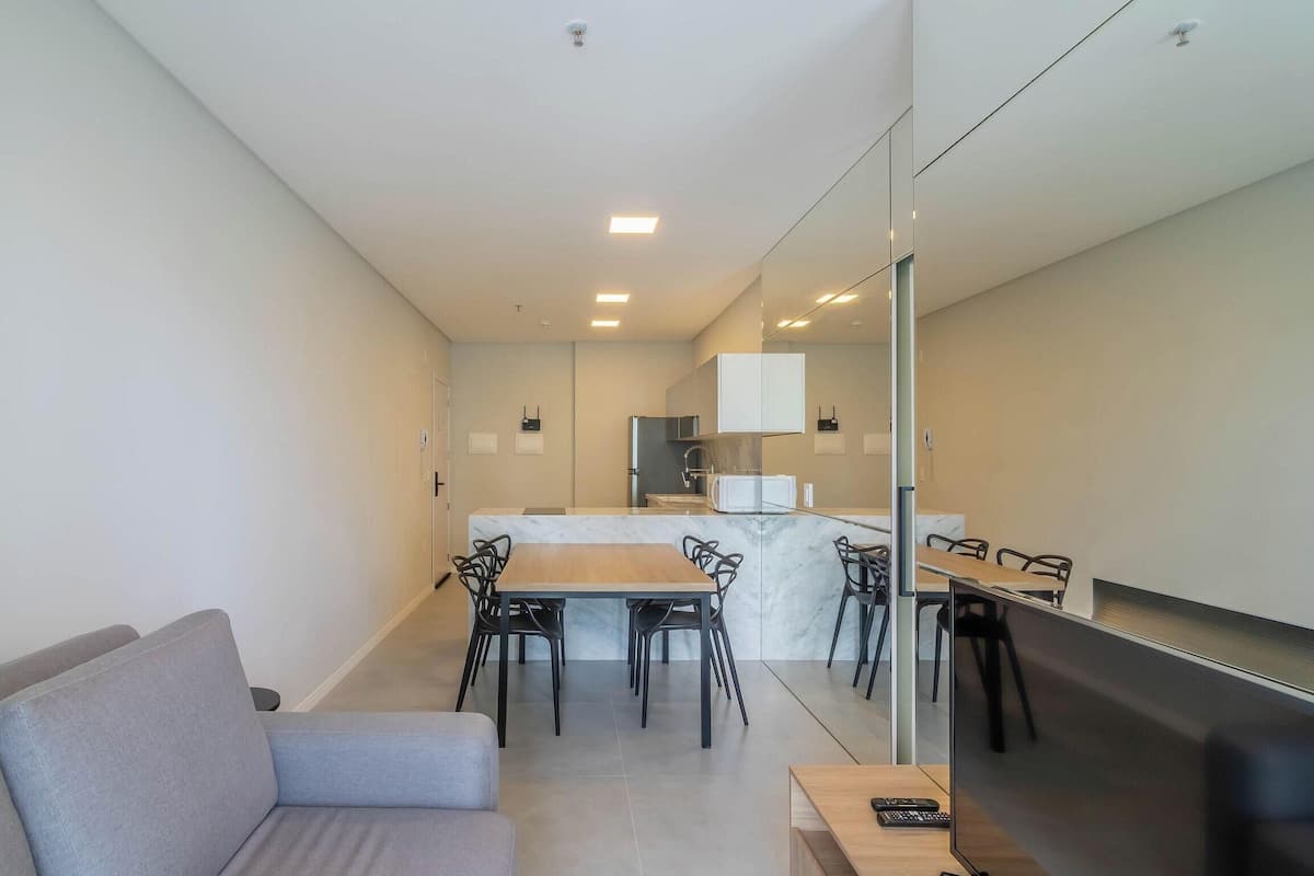 Een moderne woonkamer met een grijze bank, een eethoek met een marmeren tafel, en een keuken met witte kasten.