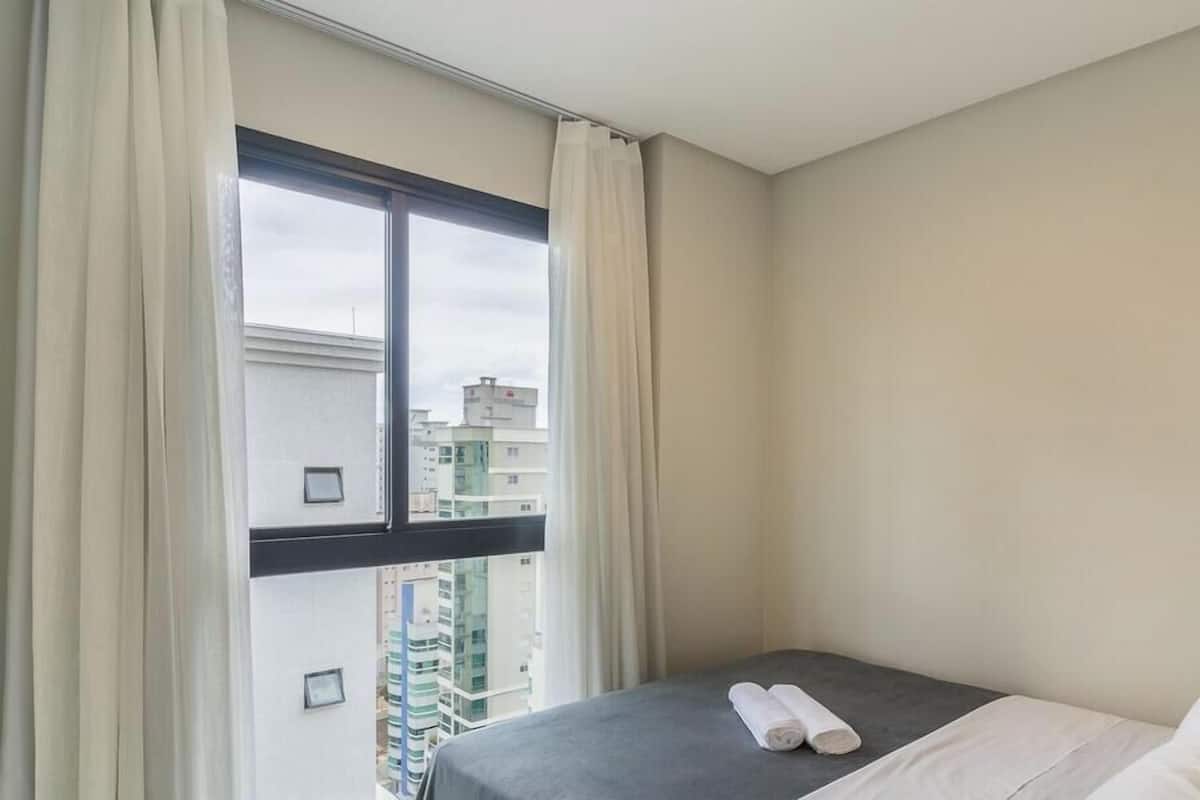 Een hotelkamer met een bed, een raam met gordijnen en uitzicht op gebouwen.