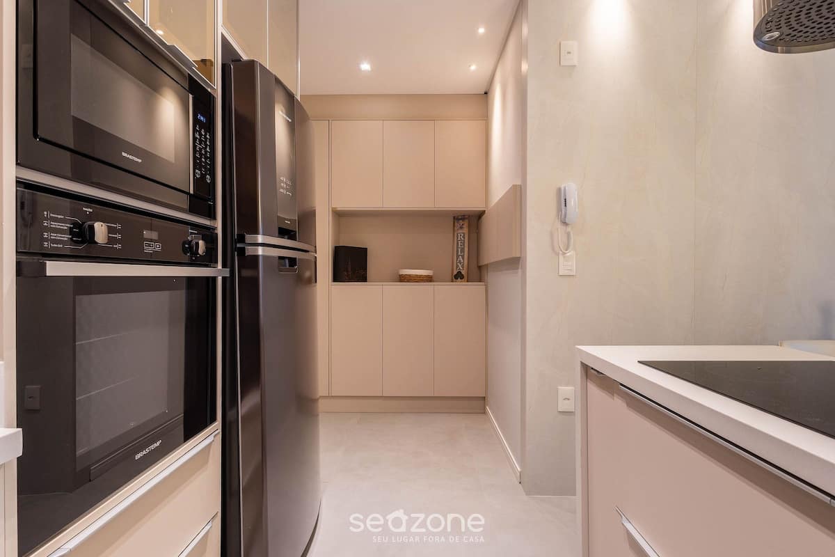 Een moderne keuken met een magnetron, oven en koelkast. Er staat een kast met een decoratief object erboven.