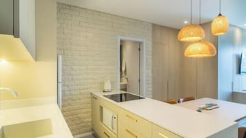Uma cozinha moderna com painel de tijolos brancos, forno embutido e bancada branca. Duas luminárias pendentes ficam suspensas acima da bancada.