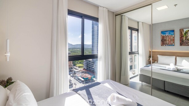 Una habitación de hotel con un ventanal grande, una cama, una mesita de noche y un espejo.
