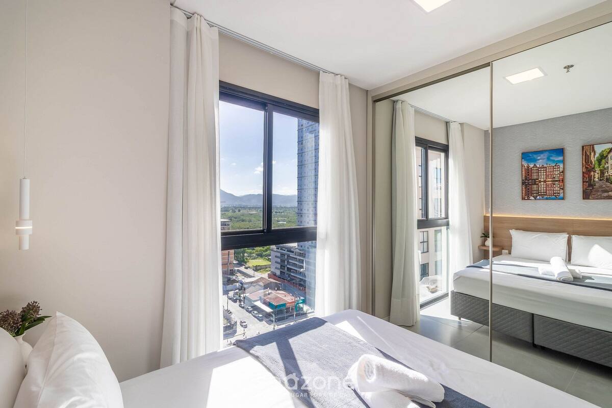 Une chambre d’hôtel avec une grande fenêtre, un lit, une table de chevet et un miroir.