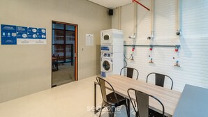 Una cocina moderna con lavadora integrada, una zona de comedor con sillas y una tubería de agua a la vista en la pared.