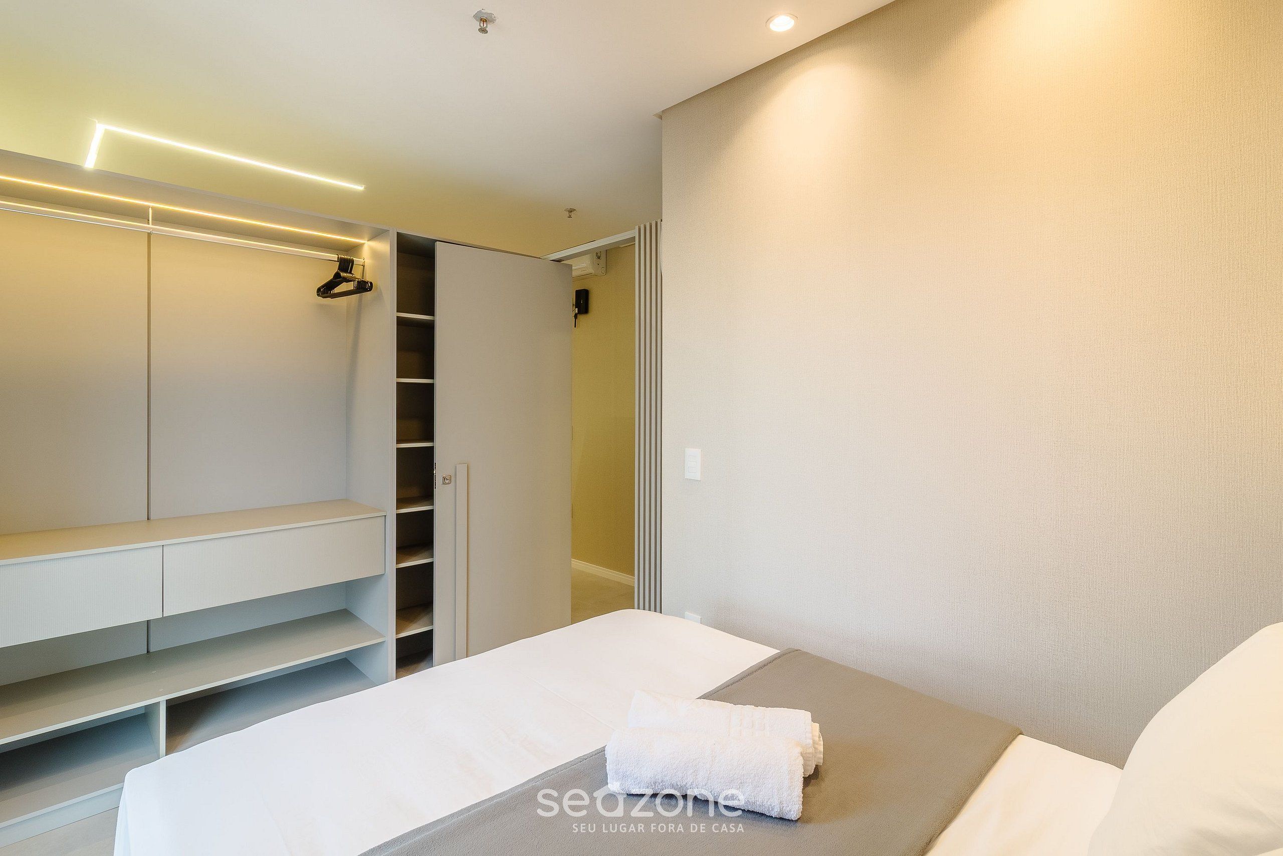 Quarto moderno com cama, roupeiro embutido e mesa de cabeceira.