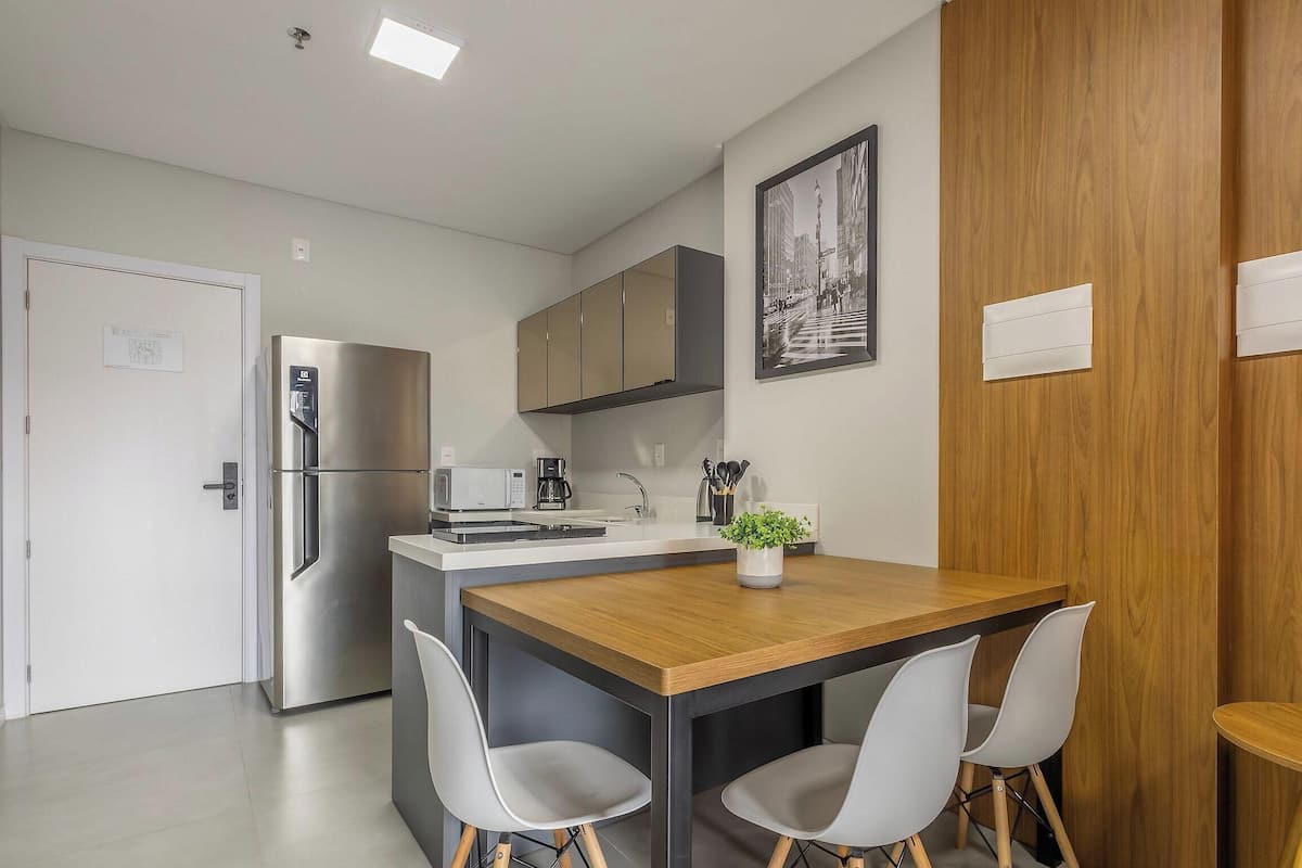 Een moderne keuken met een koelkast, magnetron en koffiezetapparaat. Er is een eethoek met een tafel en stoelen.