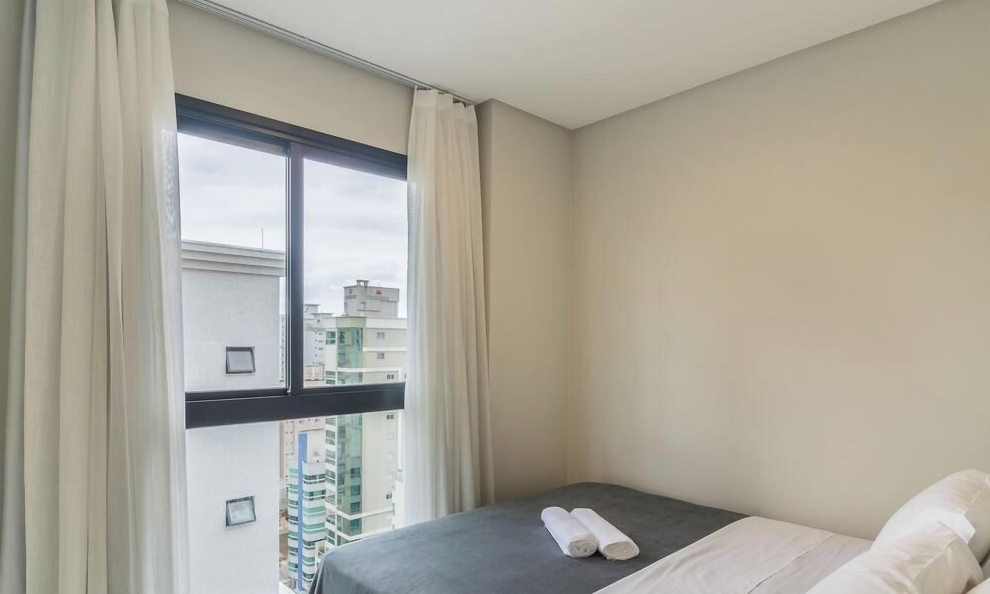 A hotel room with a bed, a window with curtains, and a view of buildings outside.