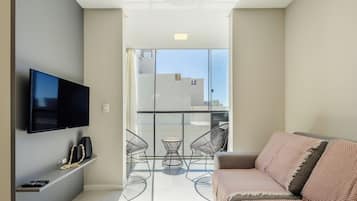 Un soggiorno moderno con televisione a schermo piatto, un divano e un balcone con vista sulla città.