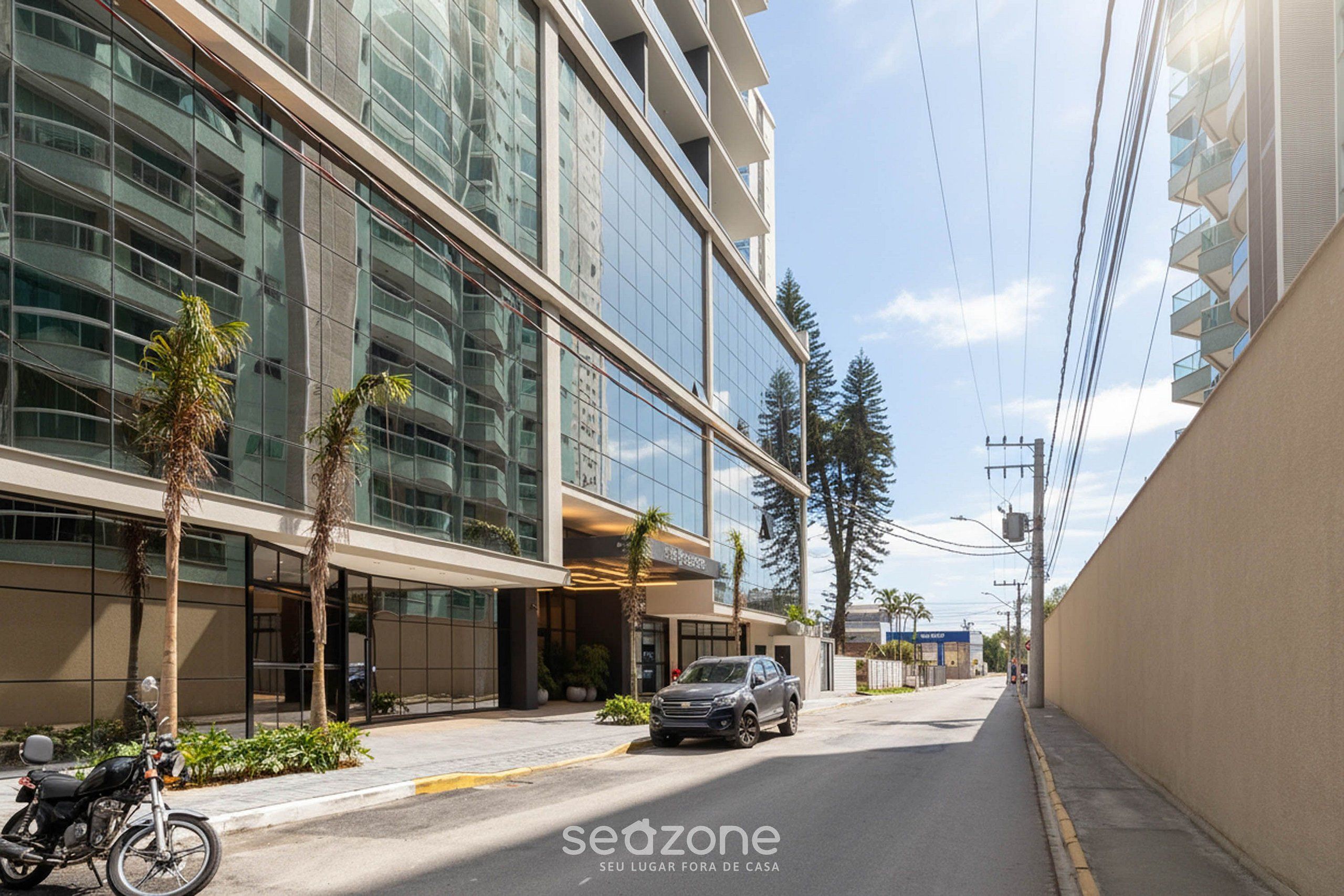 A modern building with large glass windows, a parked car, and a clear sky.