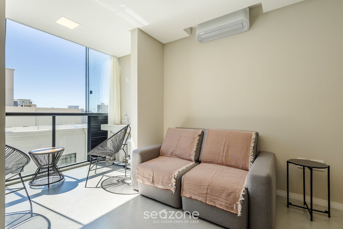 Un salon moderne avec un canapé, deux fauteuils, une petite table et une vue sur la ville.