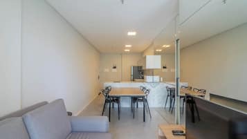 A modern living room with a sofa, a dining table with chairs, a kitchen area with cabinets, and a television.