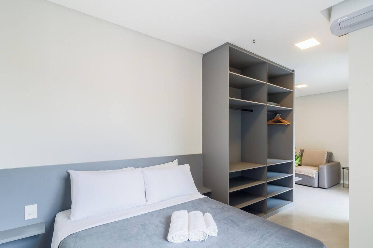 Een moderne slaapkamer met een bed, een grijze garderobe en een zithoek.