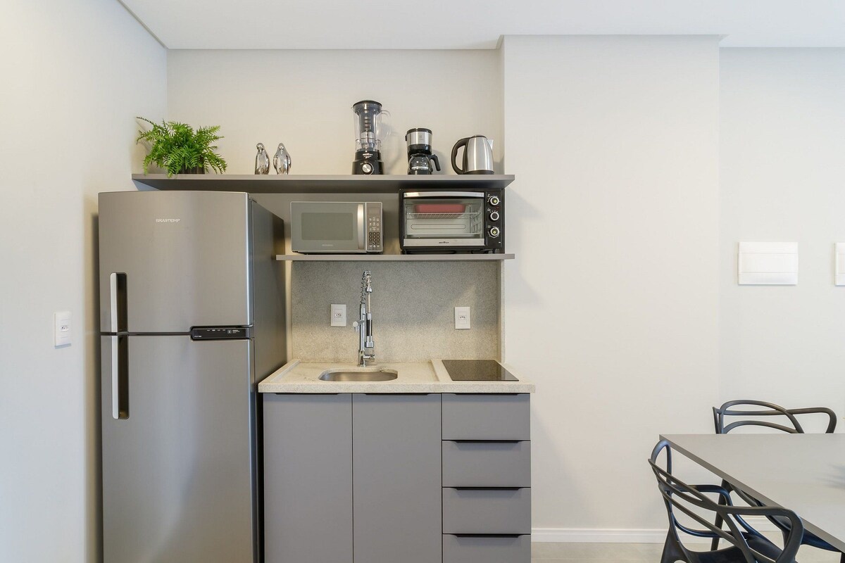A compact kitchen with a stainless steel refrigerator, a microwave, a toaster, and a coffee maker on the countertop.
