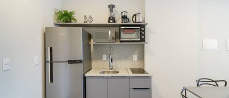 A compact kitchen with a stainless steel refrigerator, a microwave, a toaster, and a coffee maker on the countertop.