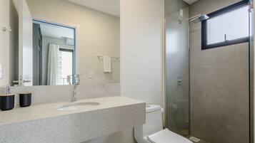Un baño moderno con encimera de granito, inodoro blanco y ducha con mampara de vidrio.