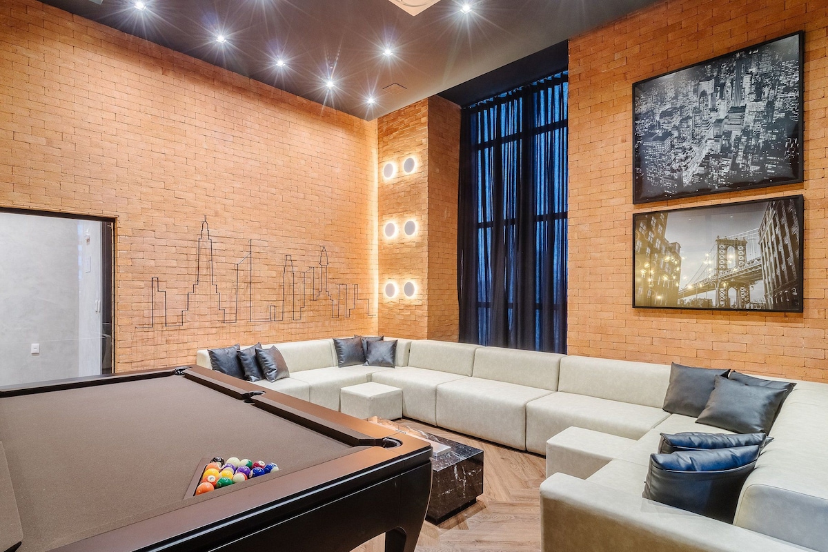 Une table de billard avec des billes, un canapé, un mur en briques et un tableau représentant un paysage urbain.