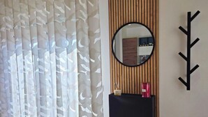 Ett rum med tunna, genomskinliga gardiner, en rund spegel, en svart hylla med diverse föremål och en väggpanel av träribbor.