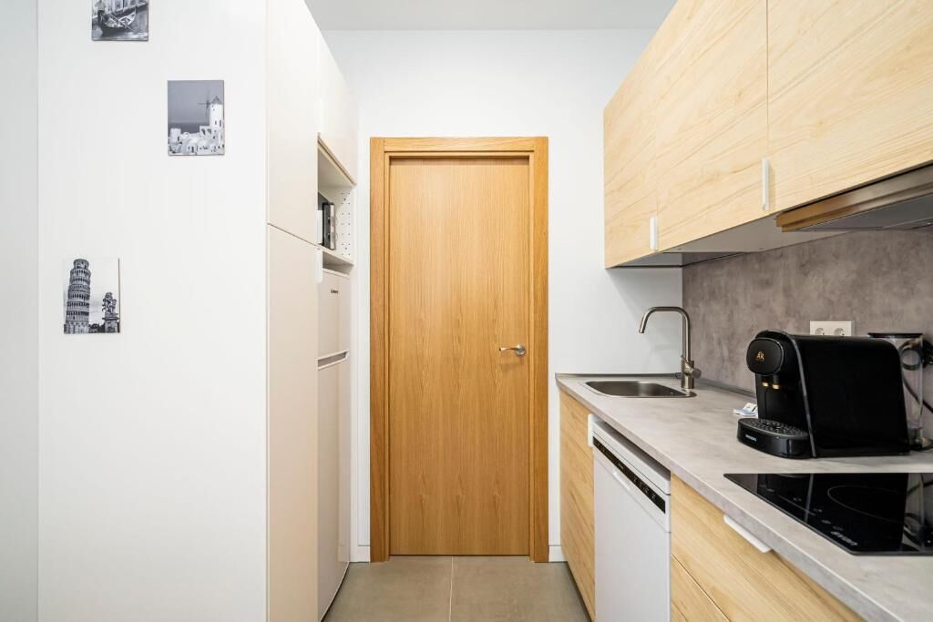 A compact kitchen with a wooden door, white cabinets, a coffee machine, and a sink.