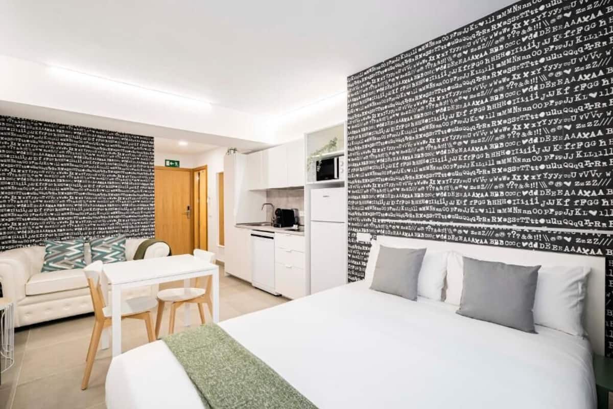 Ein modernes Hotelzimmer mit Bett, Esstisch, Sofa und einer Küchenzeile.