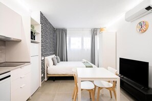 Un espacio habitable moderno y compacto con kitchenette, cama, zona de comedor y televisor.