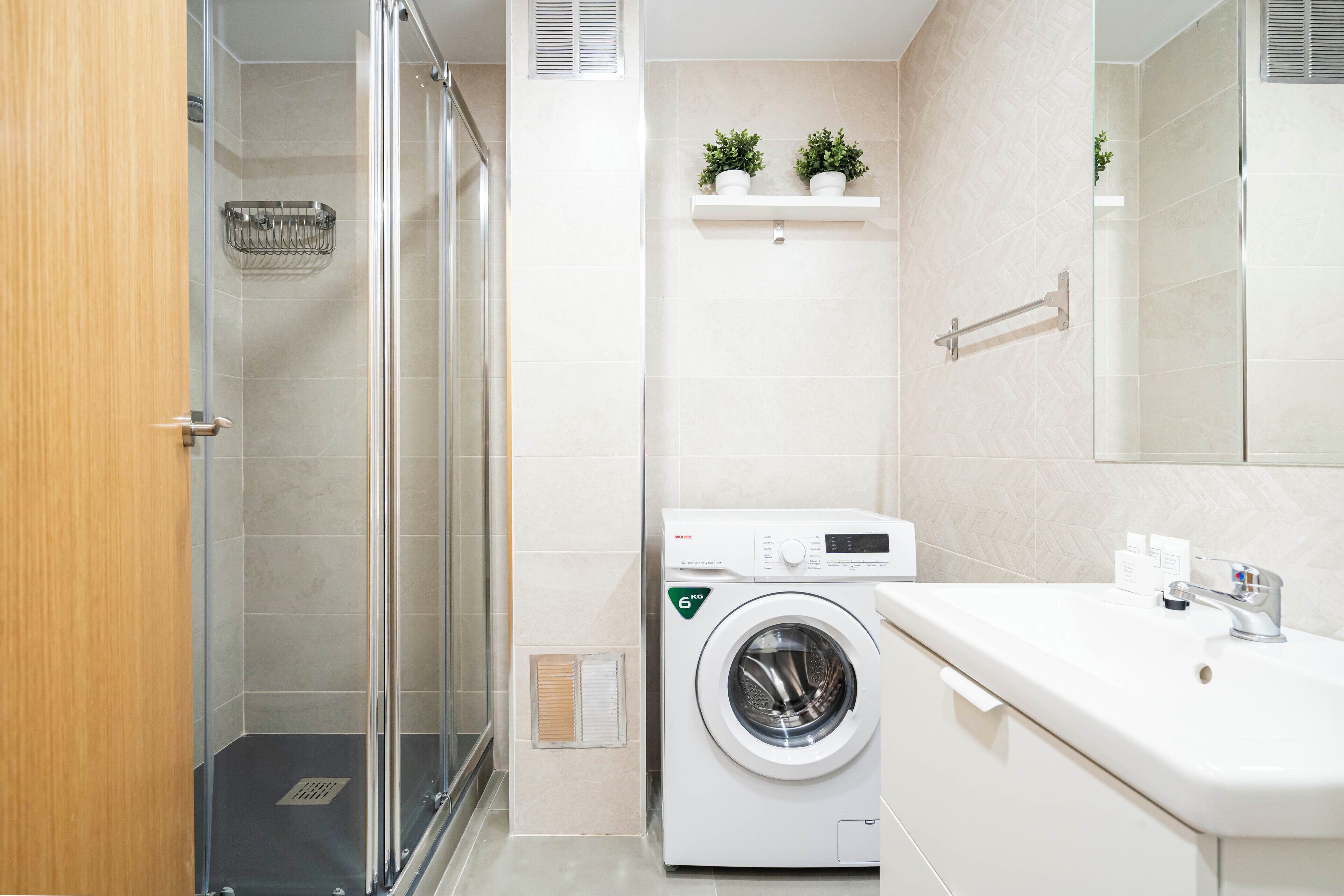 Een moderne badkamer met een glazen douchecabine, een ingebouwde wasmachine en een witte wastafel met spiegel erboven.