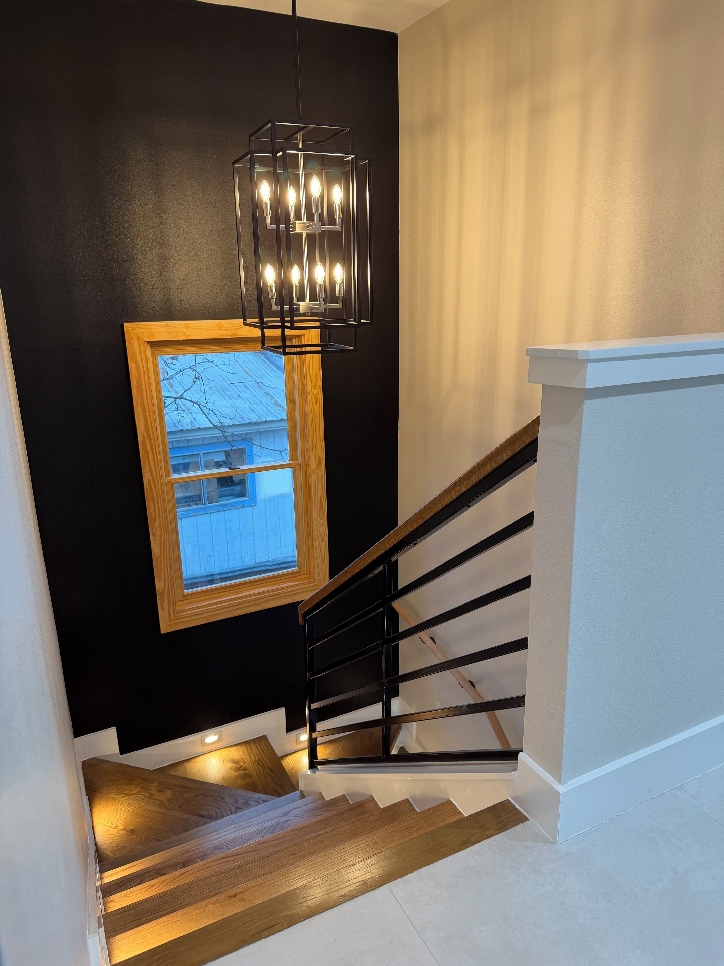 A staircase with a black wall, a wooden-framed window, and a modern light fixture.