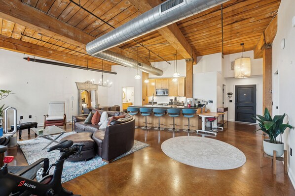 A spacious living area with a large leather sofa, a workout bike, and a kitchen in the background.