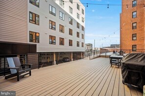 A rooftop deck with a wooden floor, outdoor seating, and a barbecue grill.