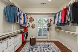 A walk-in closet with hanging clothes, a shoe rack, and a small stool. - Holly Court Hideaway Lake House on a Spacious Private Wooded Lot (Eustace)