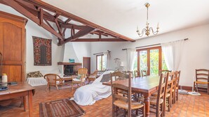 A dining area with a wooden table and chairs, a fireplace, and a view of greenery outside. - Family Home on the Edge of the Forest with Terrace, Private Garden, and Balcony (Le Grand-Village-Plage)