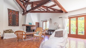 A room with a fireplace, wooden beams, a bed, a chair, and a view through a large window. - Family Home on the Edge of the Forest with Terrace, Private Garden, and Balcony (Le Grand-Village-Plage)