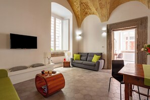 A living room with a sofa, a wooden coffee table, a flat-screen TV, and a dining table with a green table runner. - Casa Patù Appartamento storico di charme nel cuore di Napoli (Napoli)