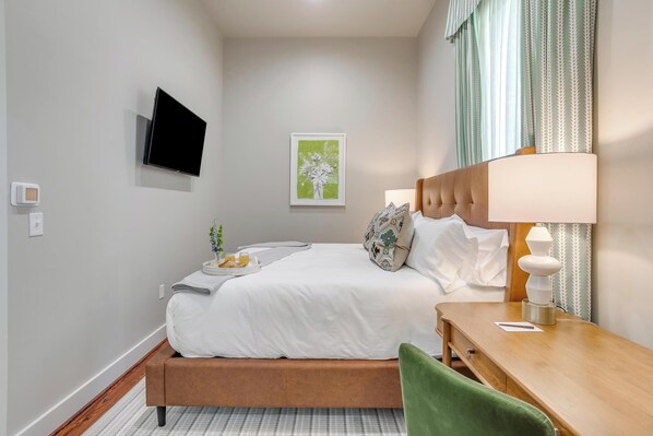 Habitación de hotel ordenada con cama, mesita de noche, lámpara y televisión en la pared.