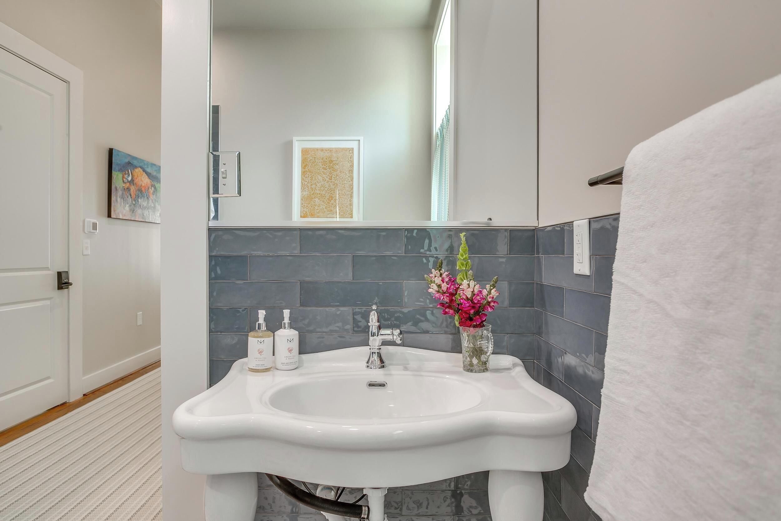 A bathroom with a white sink, two bottles of hand soap, a vase with flowers, and a towel hanging on the right.
