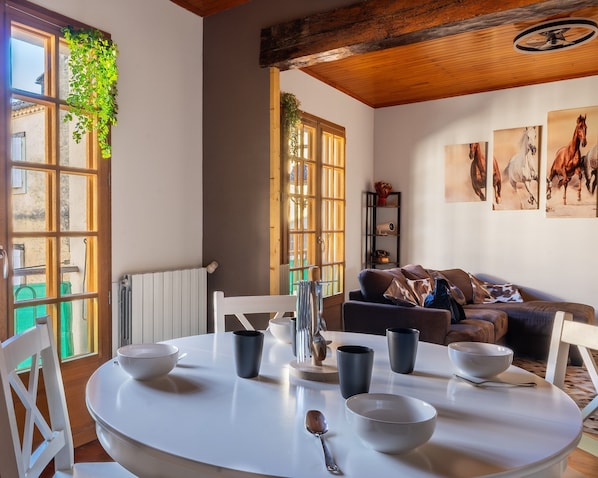 Un coin repas avec une table ronde, des chaises et des bols. Une fenêtre offre une vue sur les bâtiments à l’extérieur.
