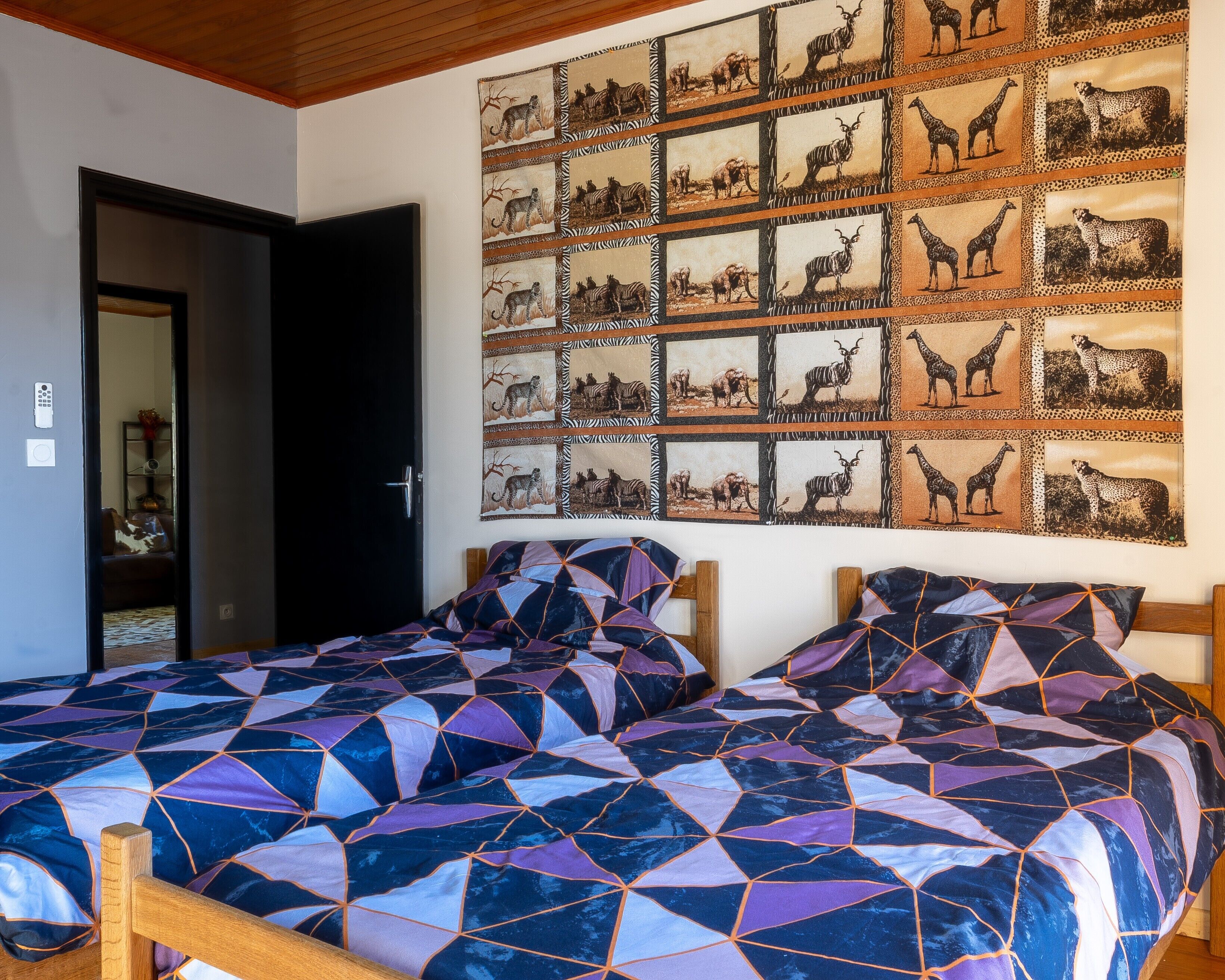 A bedroom with two beds, a wall with animal-themed artwork, and a door leading to another room.