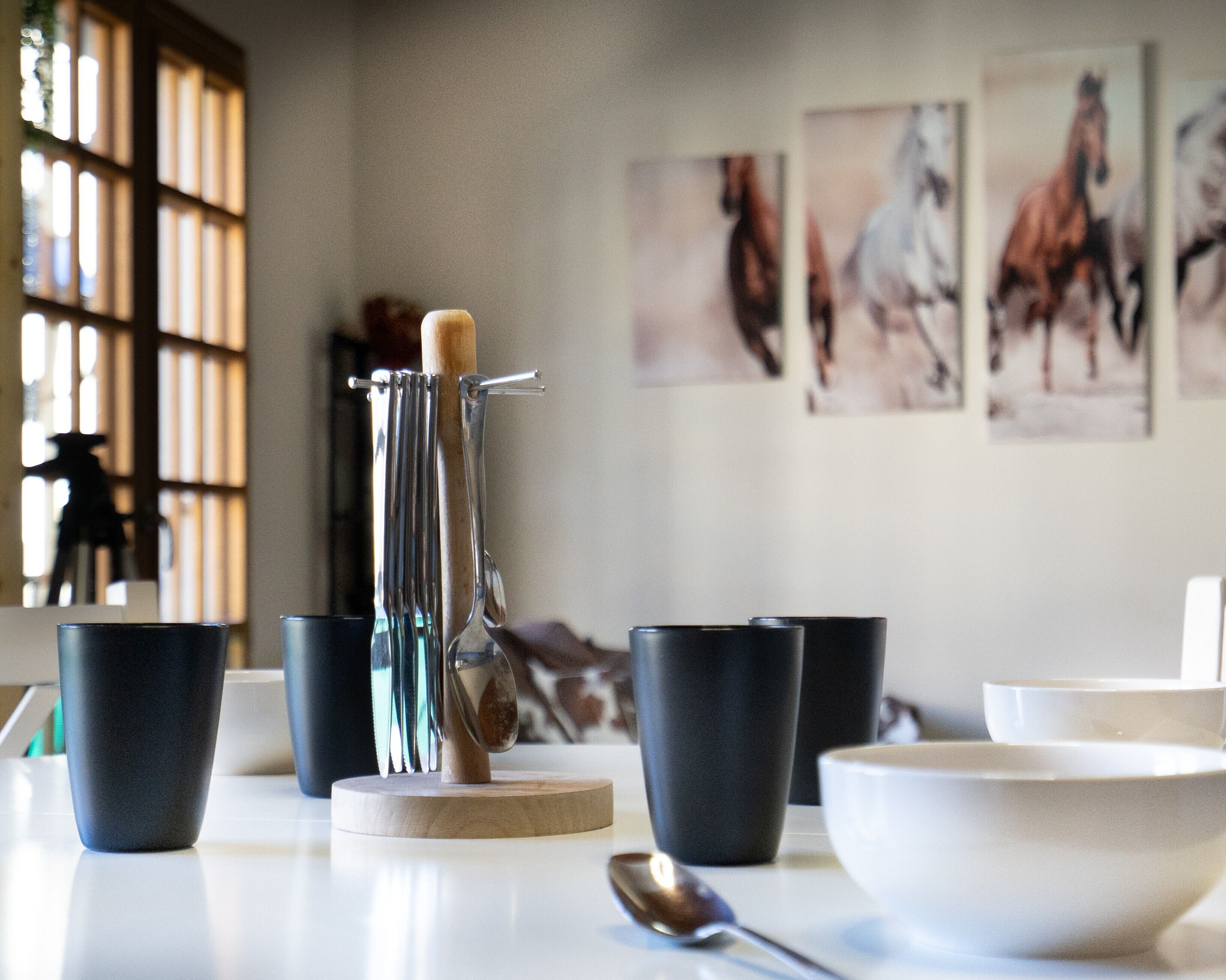A dining table with various cups and a spoon, a knife on a stand, and horse paintings on the wall.