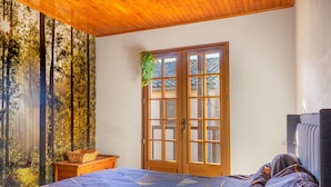 A bedroom with a bed, a wooden door, and a view of trees through a window.
