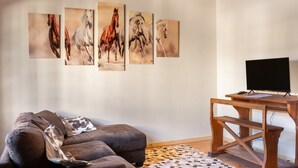 A living room with a sofa, a coffee table, a TV, and horse paintings on the wall.