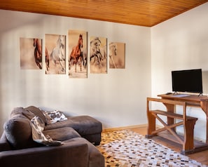 A living room with a sofa, a coffee table, a TV, and horse paintings on the wall.