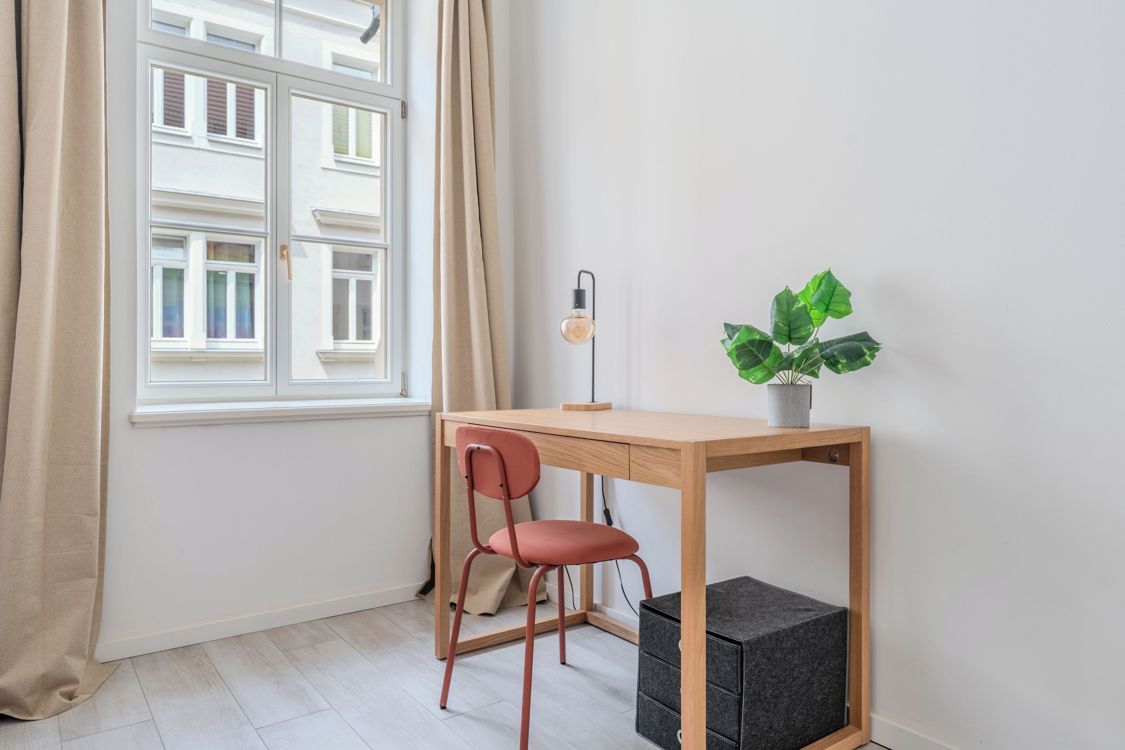 Ett rum med ett skrivbord, en stol, en krukväxt och ett fönster med gardiner.