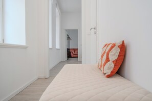 A minimalist bedroom with a bed, a pillow, and a view into another room.