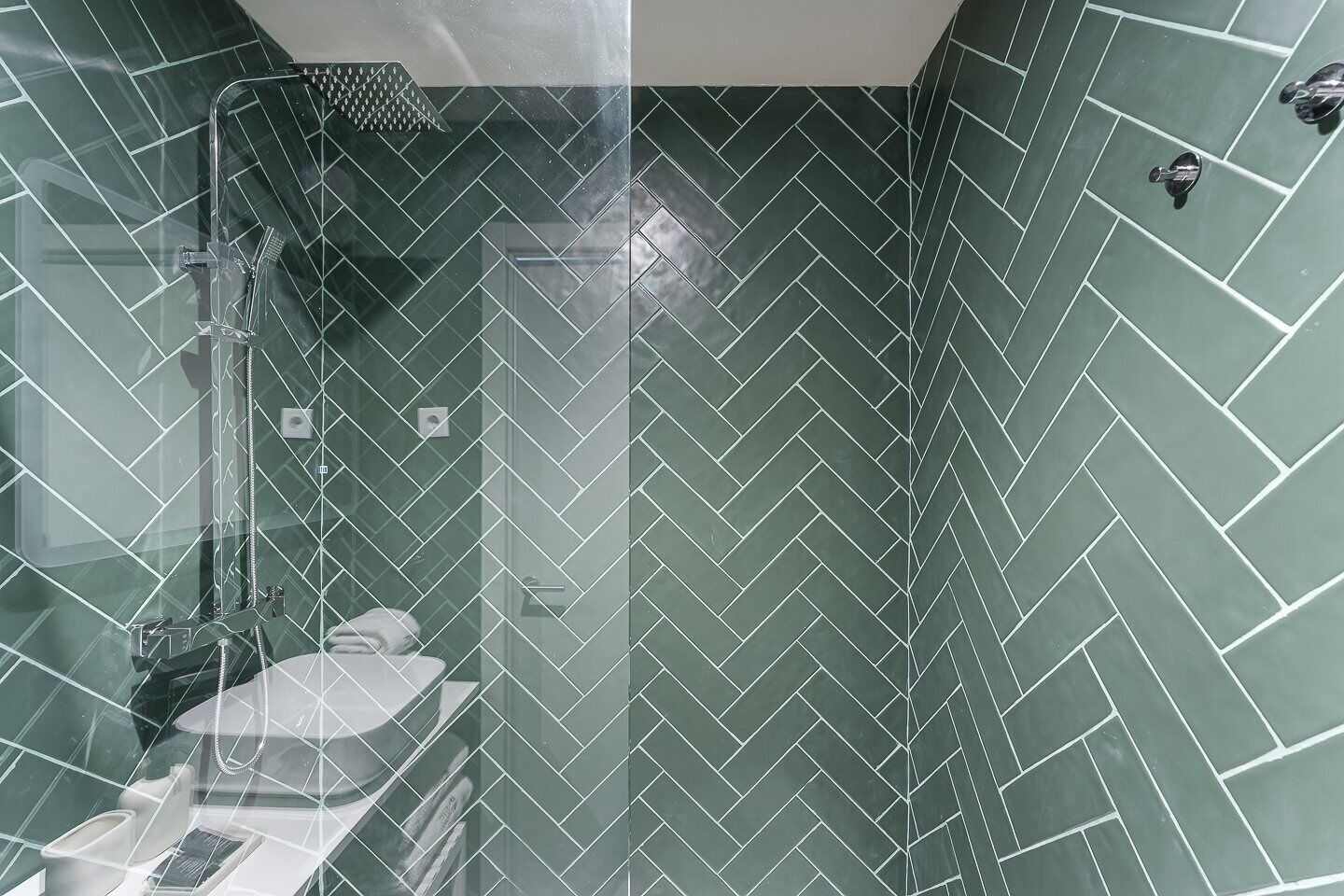 Een moderne badkamer met een visgraat mozaïek, een glazen douchecabine en een toilet.