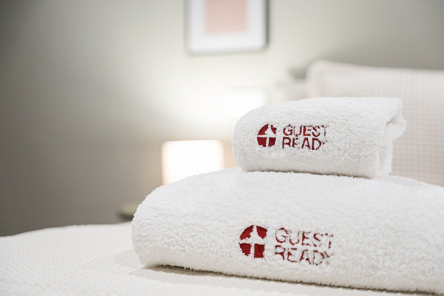 Zwei weiße Handtücher mit der Aufschrift 'GUEST READY', auf einem Bett in einem Hotelzimmer abgelegt.