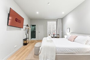 A modern hotel room with a bed, a TV, a shower, and a desk with a chair. - GuestReady - City centre stay in Porto (Porto)