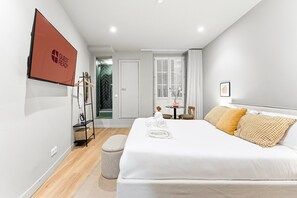 A modern hotel room with a large bed, a seating area with a table and chairs, a coat rack, and a view of the outside. - GuestReady - City centre stay in Porto (Porto)